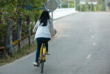 Fototapeta Miasto - a girl in a white short dress riding a yellow bicycle