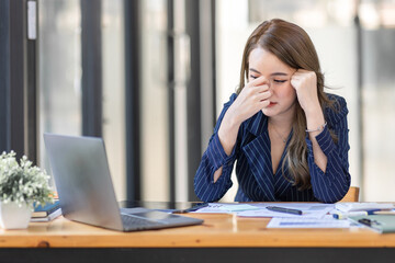 Portrait of tired young business Asian woman work with documents tax laptop computer in office. Sad, unhappy, Worried, Depression, or employee life stress concept	