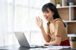© crizzystudio - happy asian businesswoman waving hand while sitting on couch and having video chat on laptop