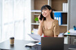 © crizzystudio - Happy young asian woman talking on the mobile phone and smiling while sitting at her working place in office.