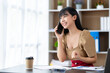© crizzystudio - Happy young asian woman talking on the mobile phone and smiling while sitting at her working place in office.