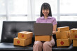 © crizzystudio - Asian women working SME business at the workplace at home. use laptop to check customer orders online shipping boxes, freelance SME entrepreneur online business idea.