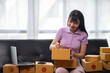 © crizzystudio - Asian women working SME business at the workplace at home. use laptop to check customer orders online shipping boxes, freelance SME entrepreneur online business idea.