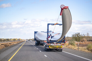 Wall Mural - Powerful big rig semi truck with additional axle dolly with oversize load sign transporting wind turbine blade running on the straight highway road