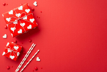 Wall Mural - Valentine's Day concept. Top view photo of gift boxes straws hearts and sprinkles on isolated red background with copyspace