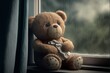 Sad and lonely toy bear sitting in a window on a rainy day alone