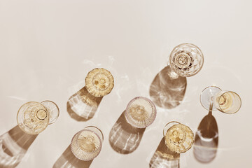 Summer party drinks flat lay, wine glasses with white sparkling wine and sunshine shadow on light table. Minimal pattern with beautiful wine glasses, above view still life, beige golden color