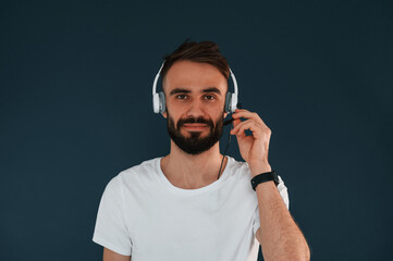 Wall Mural - In headphones. Handsome man is in the studio against blue background