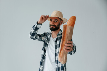 Wall Mural - Tourist in hat holding baguette. Handsome man is in the studio against white background