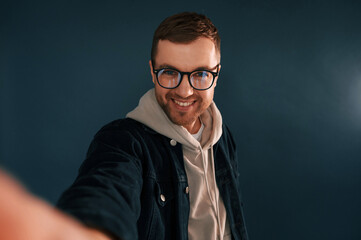 Wall Mural - Making selfie. Handsome man is in the studio against blue background