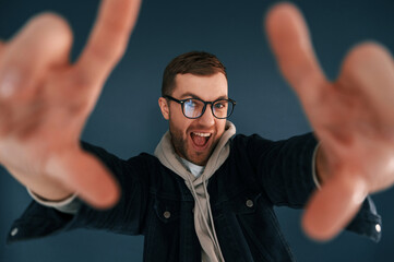 Wall Mural - Guy is pretending that he's doing photoshoot by using hands gestures. Handsome man is in the studio against blue background