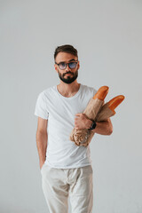 Wall Mural - Two baguettes in hands. Handsome man is in the studio against white background