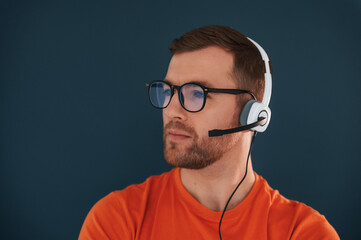 Wall Mural - Guy is in glasses and with headphones indoors. Handsome man is in the studio against blue background