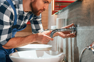 Wall Mural - Close up view. Fixing water tap. Plumber in blue uniform is at work in the bathroom