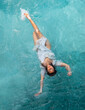 © ullision - beautiful young woman with vitiligo depigmentation in white evening dress swimming elegant floating weightless in the pool in turquoise water
