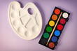 © serebryannikov - Brand new watercolor paints, brush and plastic palette on a purple background. Drawing, arts and hobby backgrounds and templates