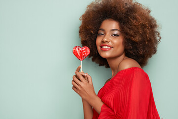 Wall Mural - Beautiful portrait of an African girl with a heart shaped lollipop. Valentine's Day. Symbol of love