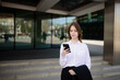 © GRON777 - A business woman near an office building using a mobile phone answers a message on the Internet, communicates with business partners.