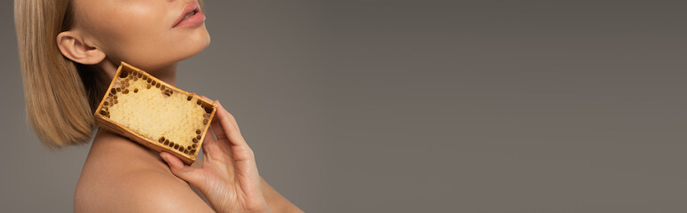 Wall Mural - cropped view of blonde young woman holding wooden frame with sweet honey isolated on grey, banner.