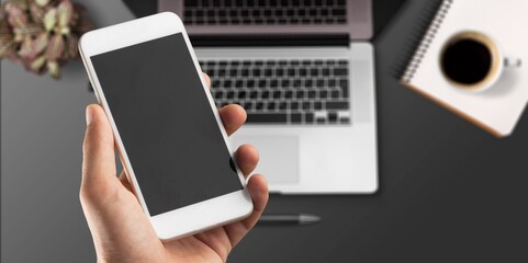 Poster - Hand holding a modern smartphone on office desk background.