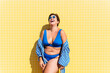 © oneinchpunch - Beautiful and confident plus size woman having fun at the beach, posing on colorful wall background - concepts about body acceptance, body positive, self confidence and body care