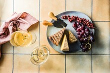 Overhead View Of A Cheese, Barberry And Grape Platter With Two Glasses Of White Wine