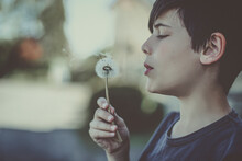 Portrait Of A Teenage Boy Blowing A Dandelion Clock, France