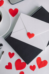 White envelope, red paper cut out hearts, office supplies, cup of coffee. Office desk on Valentine's Day. Holiday background.