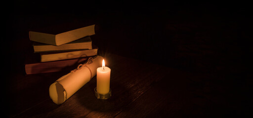 Wall Mural - Background image of old books and old paper on a wooden table in the dark under the light of a burning candle