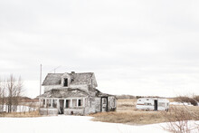 A Beautiful Run Down Abandoned Two Story House And A Camper Trailer In A Springtime Dotted With Snow Prairie Landscape