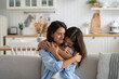 Happy smiling family of young mother and teenage daughter spending time together at home. Loving bored girl hugs woman sits on couch clinging to from behind feeling affection and not wanting to part