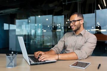 Young successful Indian programmer working inside modern development company, man using laptop to write code for software.
