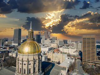 aerial shot of the golden dome of Georgia Capitol Museum surrounded by office buildings and cars driving on the street with powerful clouds at sunset in Atlanta Georgia USA