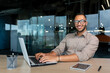 © Liubomir - Portrait of successful hispanic businessman inside office, man with laptop working typing on keyboard smiling and looking at camera.