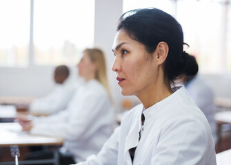 Portrait of focused female sitting at desk studying in classroom with colleagues medicals during training program for health workers