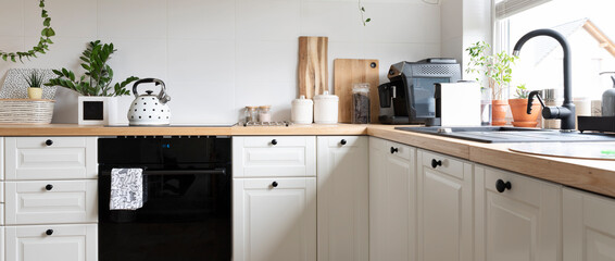 Wall Mural - Cozy interior of kitchen with sink near window, wooden counter with kettle, oven and white kitchen furniture. Banner.