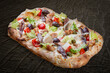 Caesar pizza with chicken, anchovies, romaine, cherry, kalamata, capers, pesto. Roman pizza rectangular on wood background