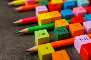 Many colorful cubes with numbers, multiplications and pencils on dark grey table, closeup
