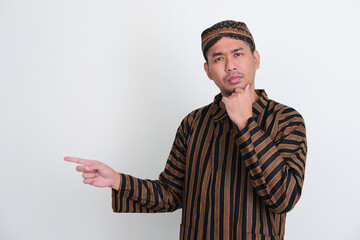 Wall Mural - Asian man wearing traditional Javanese costume pointing to the right side with thinking expression