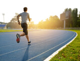 Fototapeta  - A man running on athletic track with sunrise background...