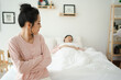 © DG PhotoStock - Unhappy - stressful Asian woman sitting and crying on the bed while her husband sleeping, a family and post marriage problem. Arguing Asian young couple with bad - negative relationship.