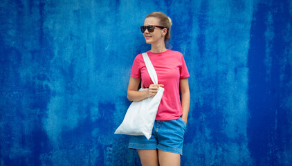 Wall Mural - Female model wearing pink blank t-shirt on the background of an blue wall.