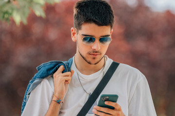 Wall Mural - portrait young man walking with mobile phone and sunglasses in summer