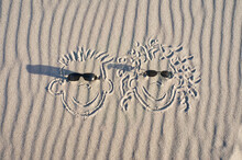 Face Drawn In The Sand On The Beach, With Sunglasses. Sand With Wave Pattern