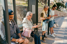People Waiting In Bus Stop Checking Their Smartphones