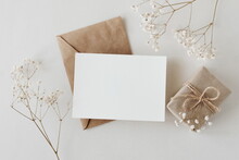 Greeting Card Mockup, Envelope, Gift Box And  Dried Gypsophila Flowers Twigs On Beige Background Top View Flatlay. Card Mockup With Copy Space.