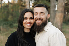 Portrait Of Happy Young Woman And Man Looking In Camera Enjoy Romantic Date In Park. Smiling Bearded Man And Brunette Girl Feeling Happiness Outdoors. Romantic Couple Enjoying Leisure Time Together.