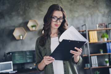 Photo of serious busy lady programmer wear glasses reading documents checklist indoors workstation workshop