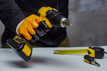 Male worker holds a close-up electric cordless screwdriver in his hands against the background of a construction tool and a concrete wall.