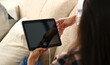 © H_Ko - Woman is holding tablet while sitting on couch
